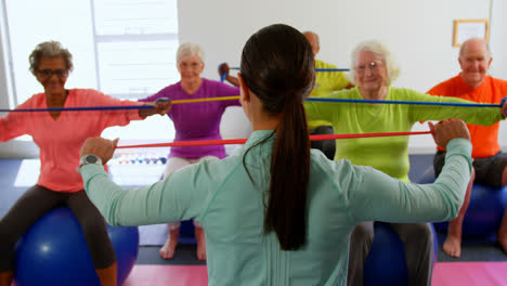 Rear-view-of-female-trainer-training-senior-people-in-exercise-at-fitness-studio-4k