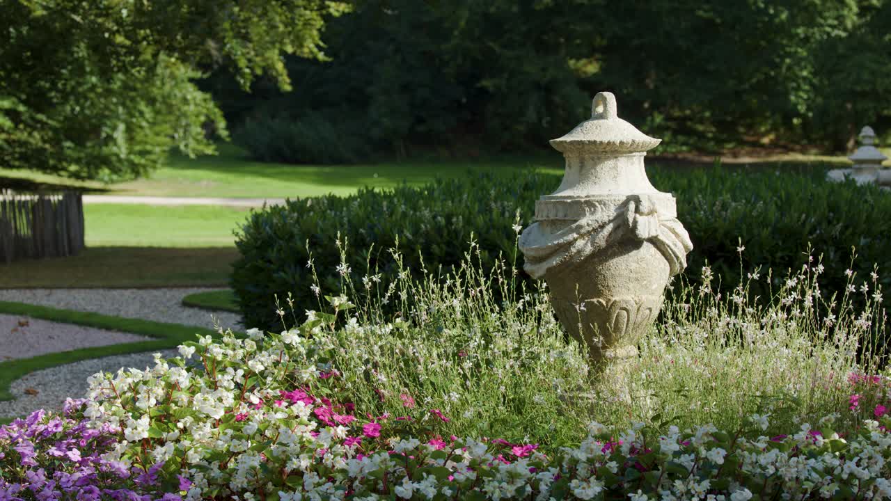 Stone statue surrounded by blooming flowers, greenery, and insects in a peaceful garden