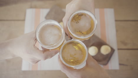 overhead view of three people toasting with glasses of beer and enjoying traditional chipa bread on a wooden table with a striped tablecloth