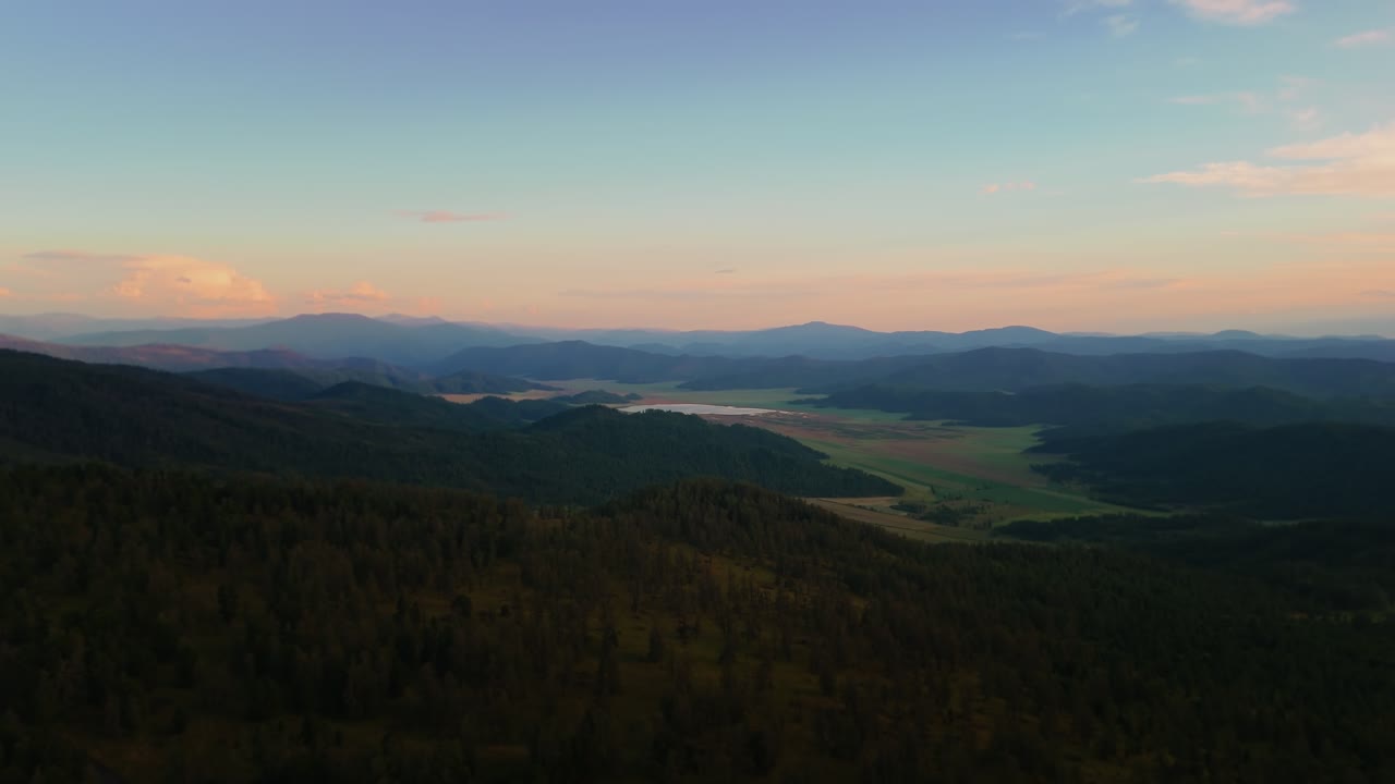 Aerial drone view of cloudy hills with forest and valleys at sunset with warm sky colors. Scenic wilderness landscape ideal for travel, nature, environment, and relaxation themes