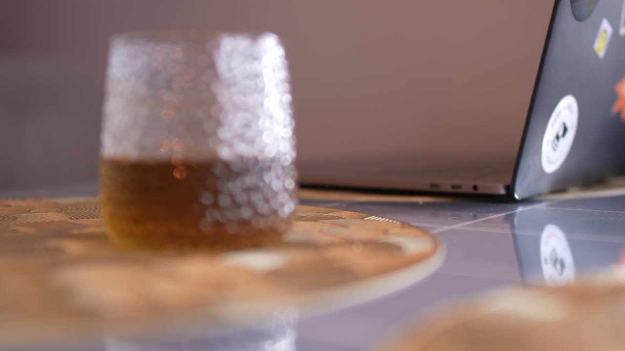 Close-up of a glass with tea placed beside a laptop on a modern table, creating a calm work-from-home atmosphere