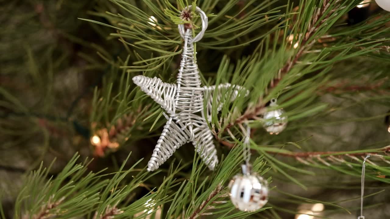 A silver star Christmas decoration made of wood hanging on a pine tree with lights