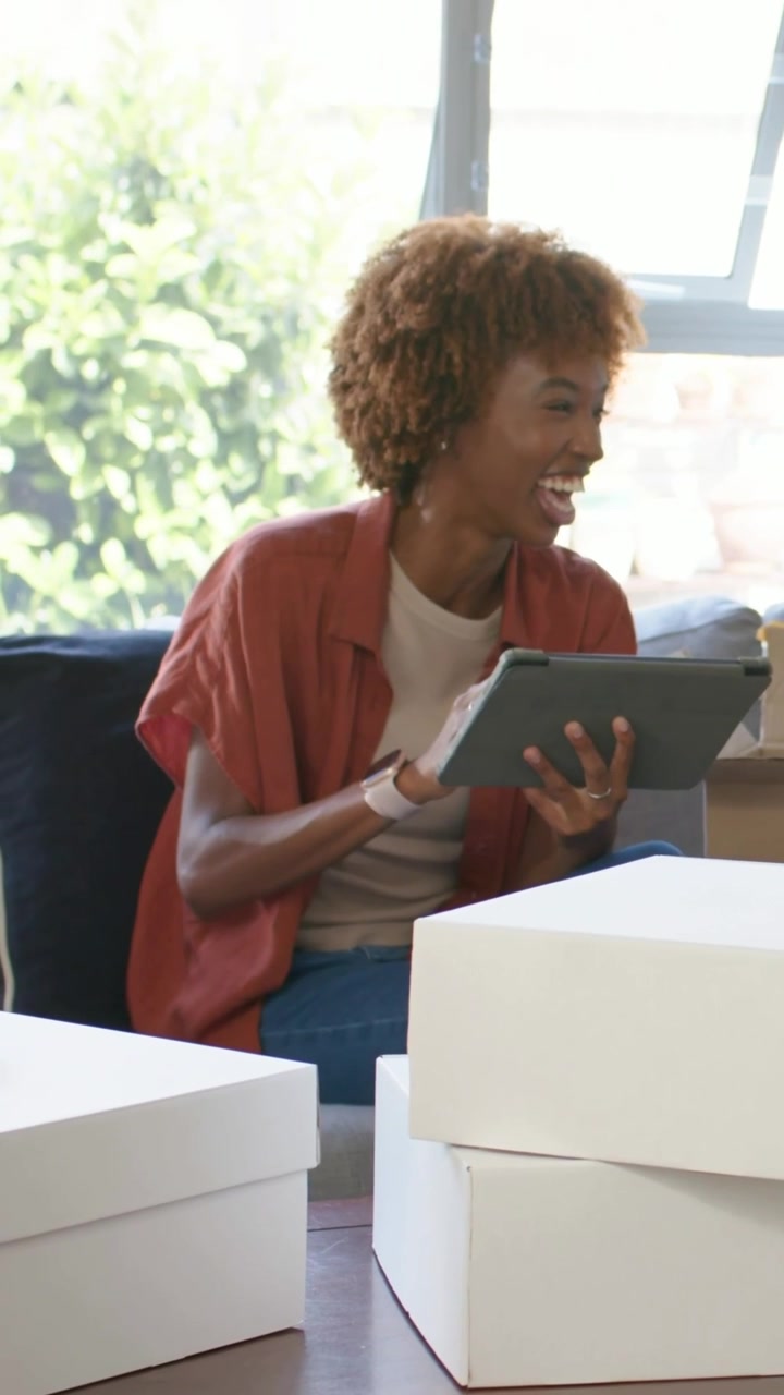 Woman seller tapping tablet in home studio, animating labels onto white boxes, managing orders