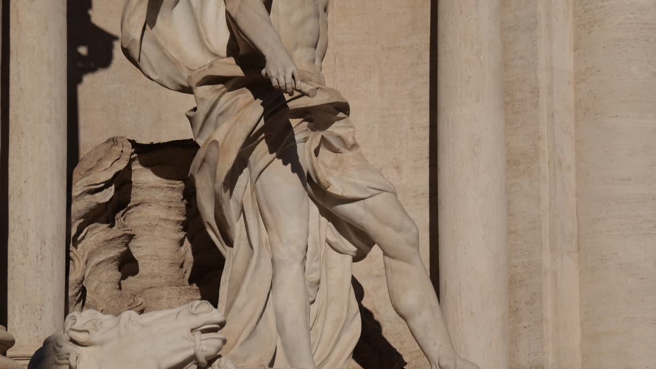 Tilt up on the Oceanus statue at Rome’s Trevi Fountain, starting from the feet and rising to the upper torso and head, highlighting dynamic baroque sculpting in sunlight.
