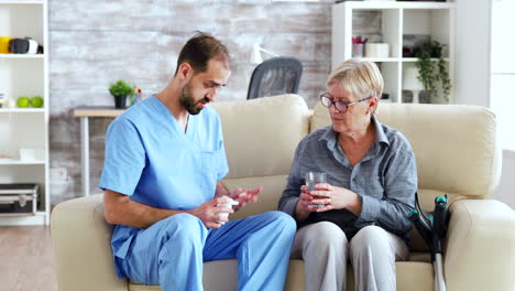 enfermera masculina sentada en el sofá con una mujer mayor dándole tratamiento médico en un hogar de ancianos