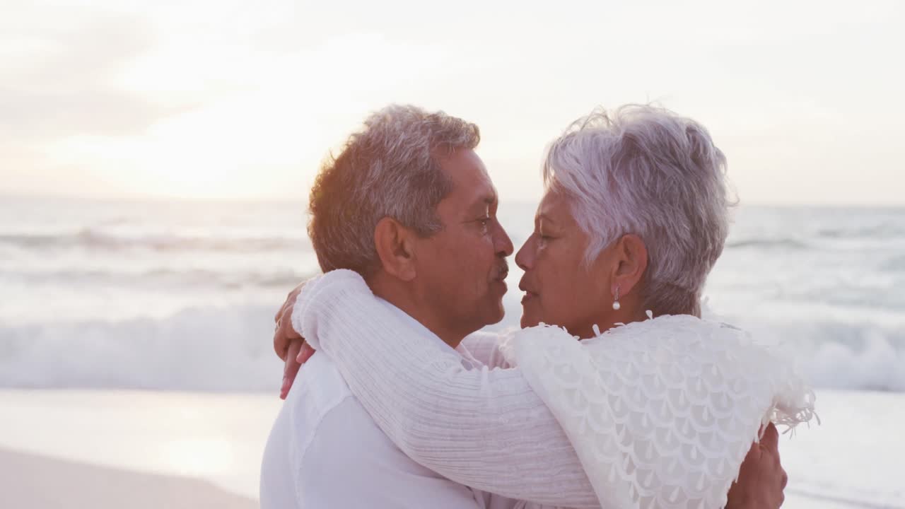 feliz hispano recién casado pareja de último año besándose en la playa al atardecer