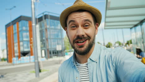 Close-up-view-of-Caucasian-young-happy-man-traveller-talking,-waving-hands-and-smiling-at-the-camera-outdoors-in-summer