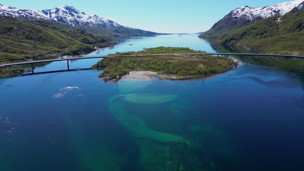 Turquoise water reflects mountains in a fjord of the Lofoten Islands, Norway, with a bridge connecting two islands
