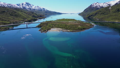 turquoise water reflects mountains in a fjord of the lofoten islands, norway, with a bridge connecting two islands