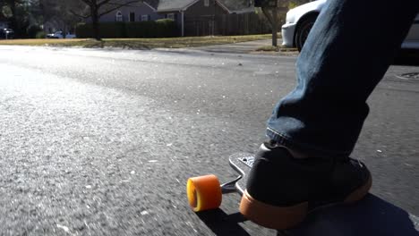 Nahaufnahme-Eines-Skateboards-Und-Der-Füße,-Während-Eine-Person-Mit-Ihrem-Langen-Brett-Eine-Straße-Hinunterfährt---Zeitlupe