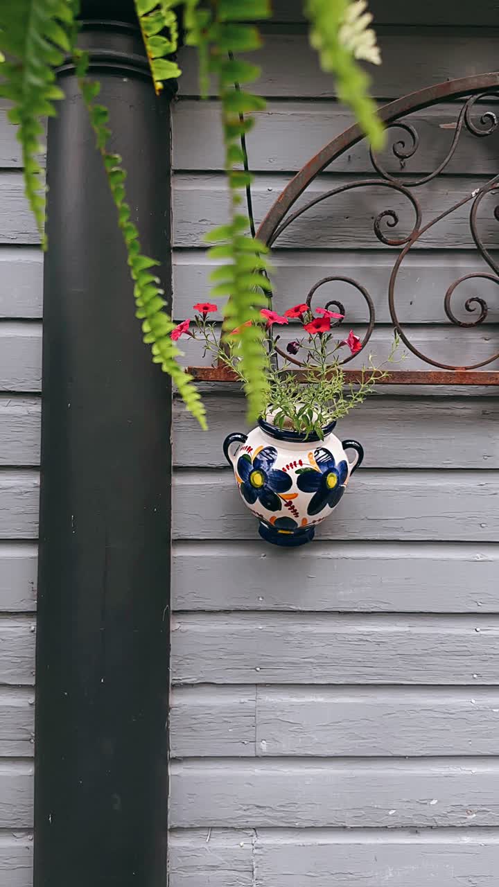 una olla de flores decorativas colgando de una casa gris