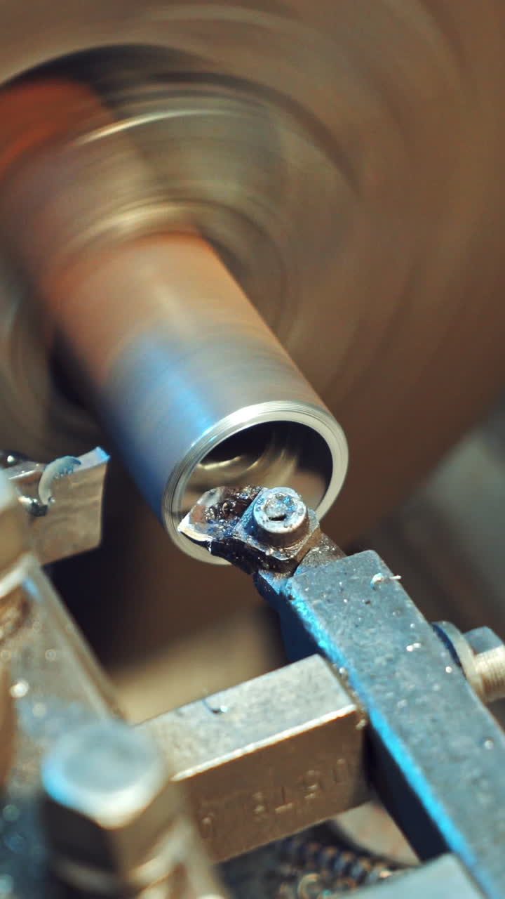 A metal shavings are falling to the floor during processing of part on the lathe in the production. Close-up. Vertical video