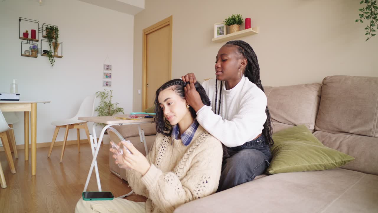 Two friends braiding hair at home
