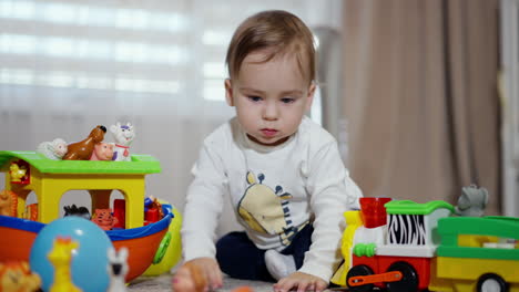 adorable little baby boy sitting among the bright toys indoors. toddler leaves his toys and crawls approaching camera.