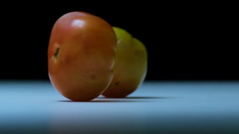 Filmische-Zeitlupenaufnahmen-Von-Alten-Tomaten,-Die-Auf-Einer-Arbeitsfläche-Gerollt-Werden,-Sauberer,-Scharfer,-Dunkler-Hintergrund