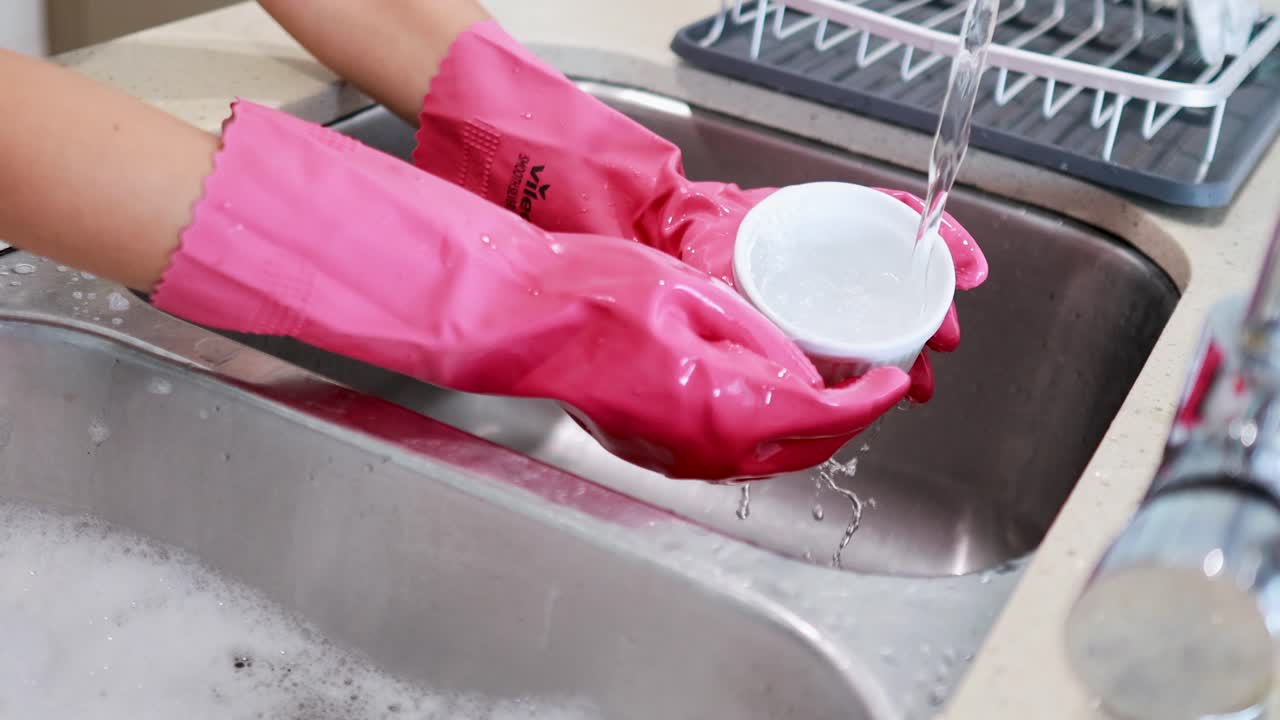 Hands in pink gloves wash a dish under running water in a kitchen sink