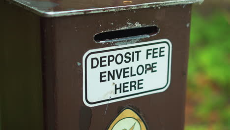 closeup of heavy duty outdoor campground cash money fee collection post with deposit envelope slot sign at camping site in nature