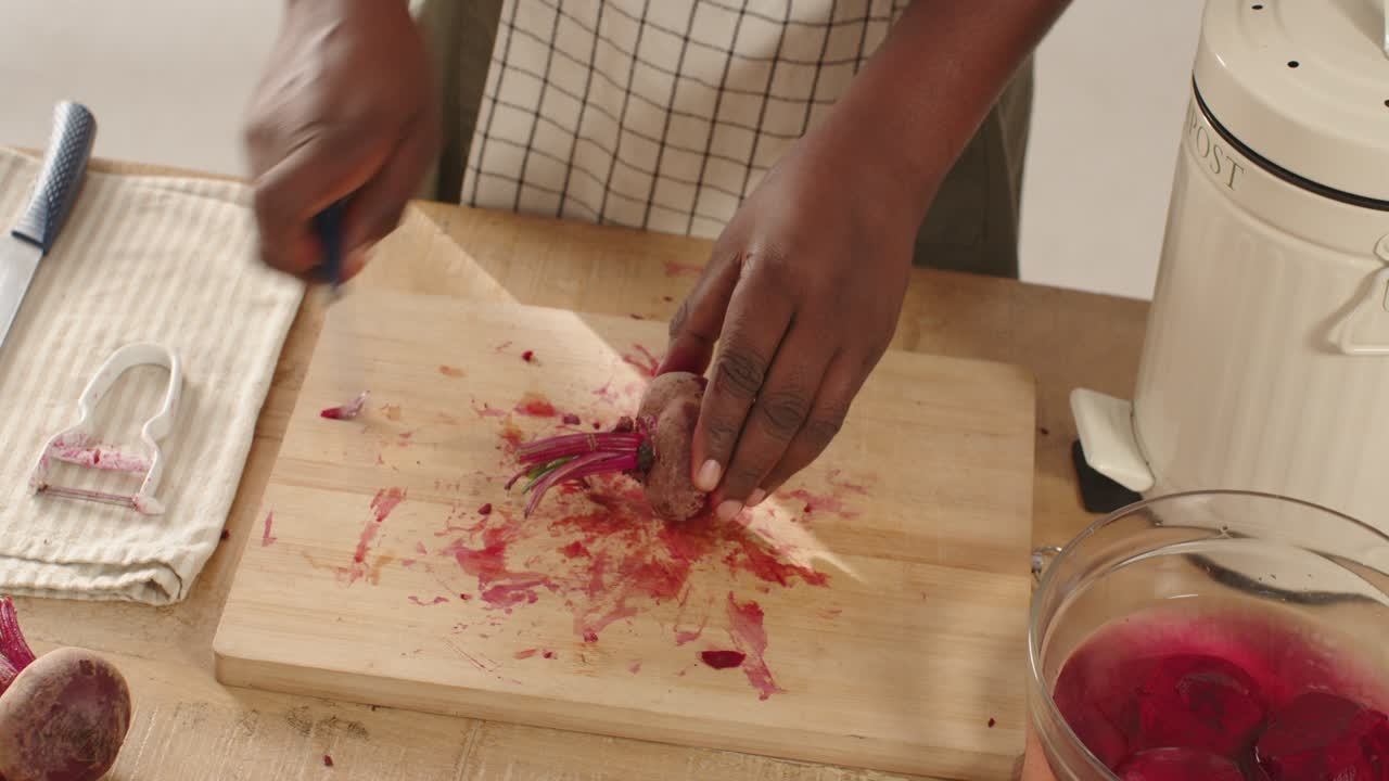 African midadult male holding beet peeling at kitchen on board with peeler cutting with blue knife