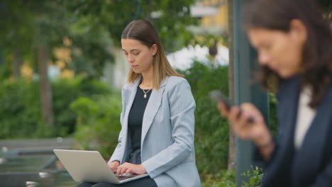 female office workers outdoors working on laptop and using mobile phone during break from the office