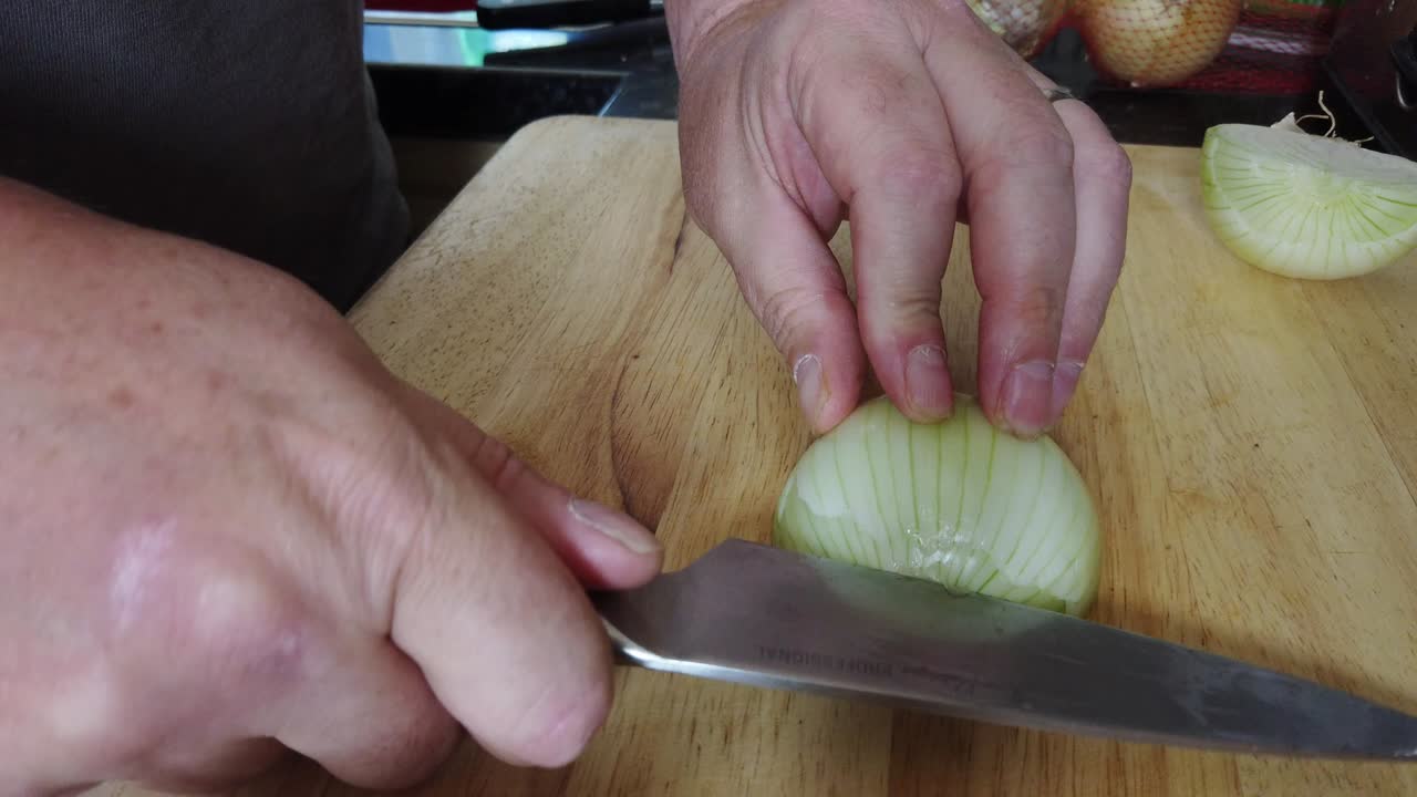 A man demonstrates how to finely dice a large white onion in a home kitchen