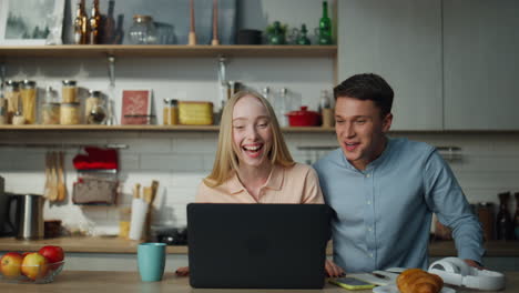 Happy-couple-greeting-webcam-speaking-with-friends-by-video-call-at-home-kitchen