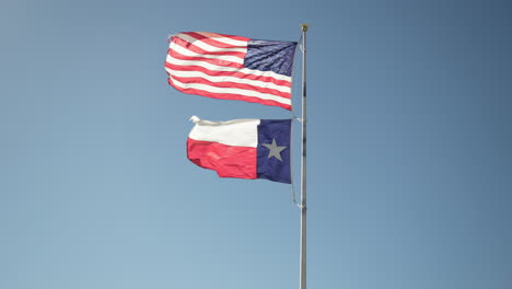 united states of america flag and texas flag flapping in the wind on a flagpole