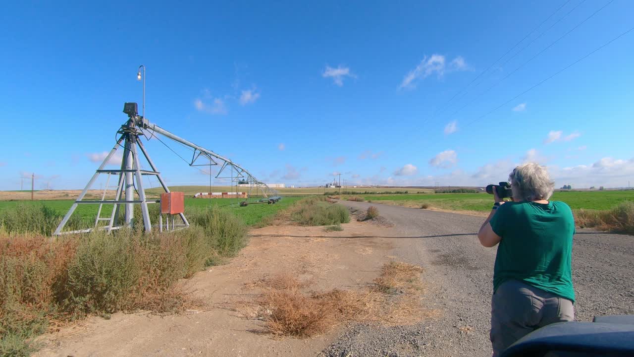 Female photographer taking pictures of a pivot irrigation head at the edge of a field