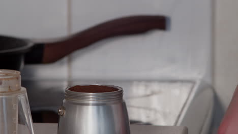 hand places ground coffee trivet into moca pot of water