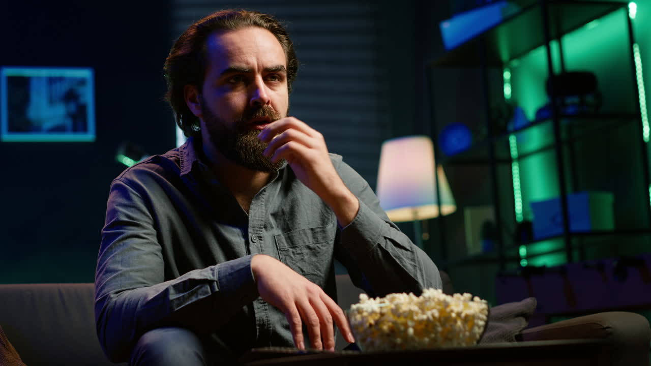 hombre desconcertado comiendo palomitas de maíz mientras ve una película confusa en la televisión