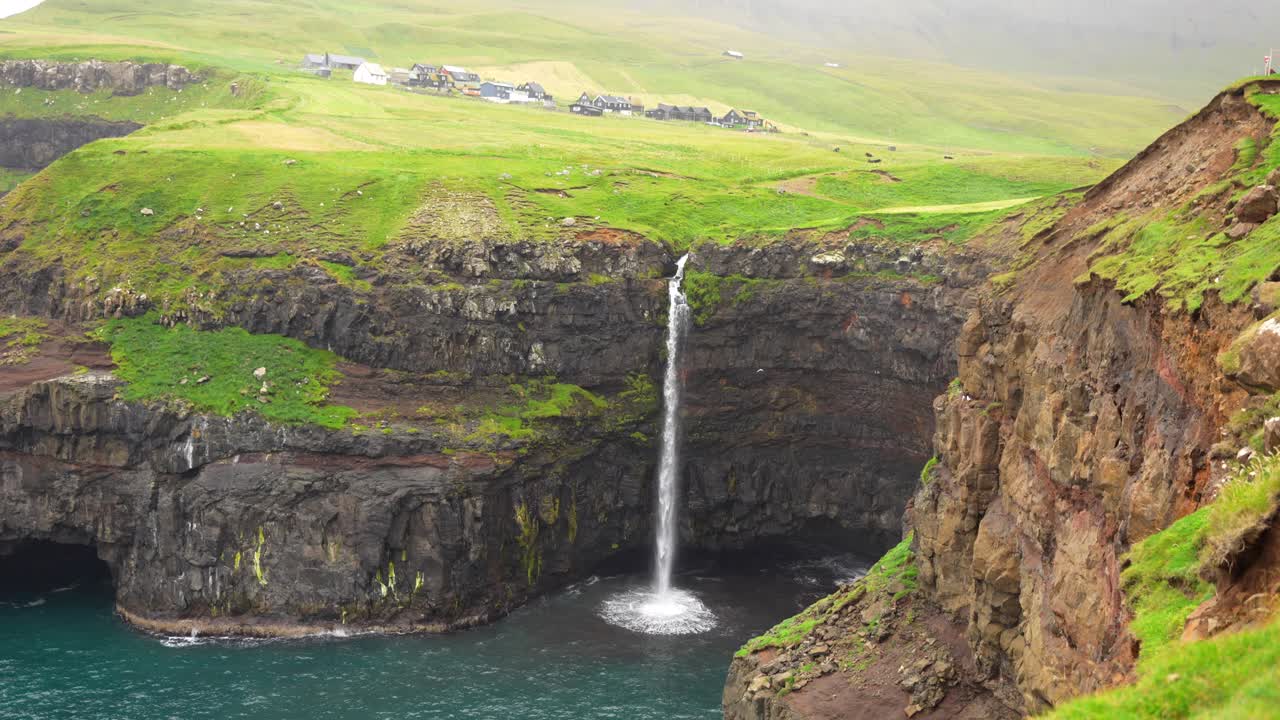 impresionante toma de telefoto de la cascada de mulafossur cayendo en el océano, faroe