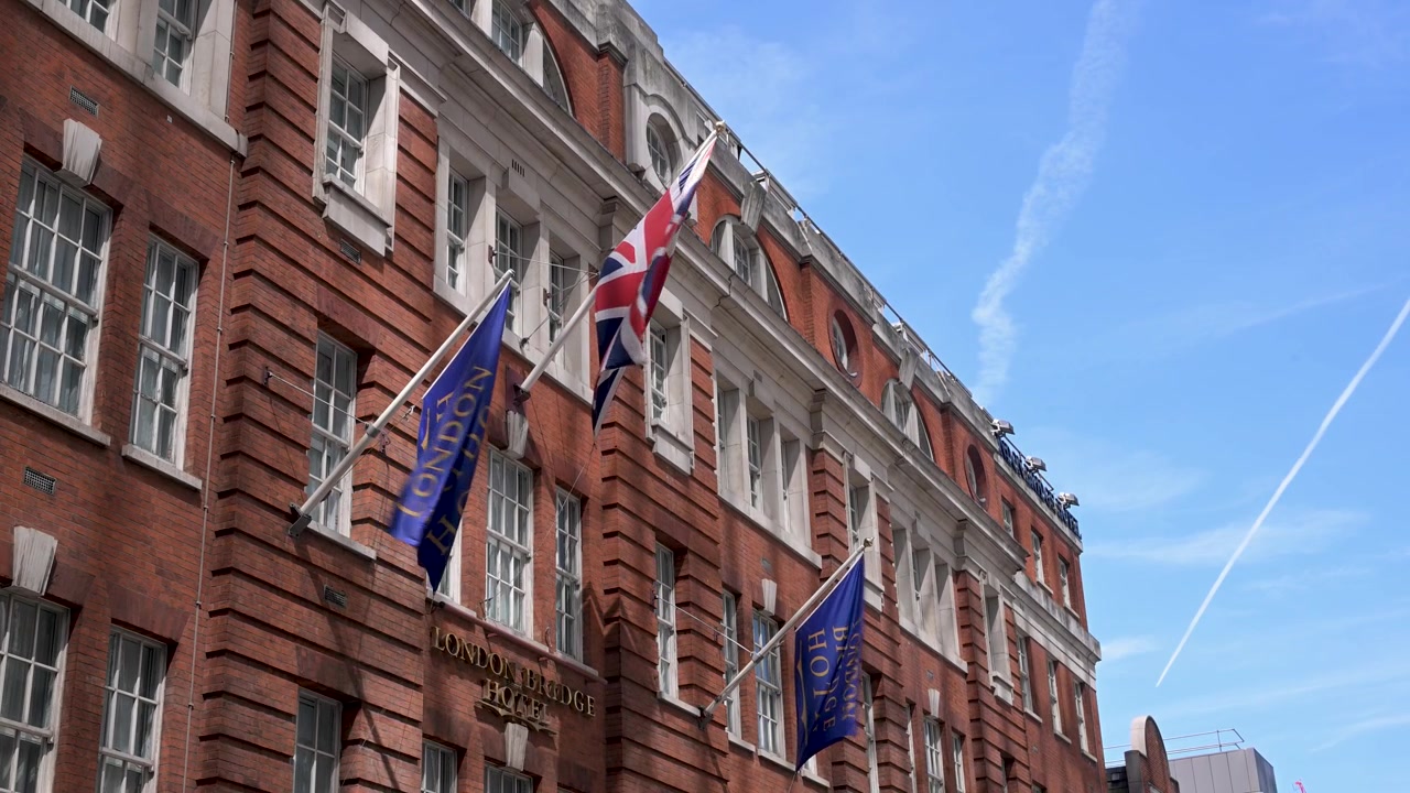 Flagi Union Jack i hotelowe powiewają na wietrze na fasadzie hotelu London Bridge z czerwonej cegły pod jasnym, błękitnym niebem