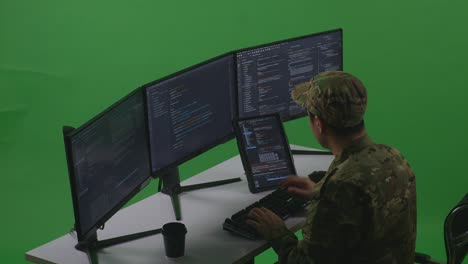 vista lateral del desarrollador soldado asiático trabajando con una tableta mientras escribe código con múltiples pantallas de computadora en el estudio de pantalla verde