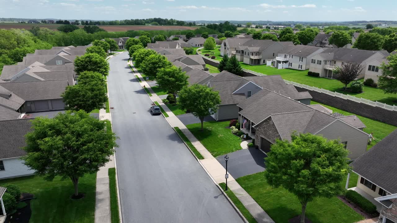 Tree-lined street of upper class housing area in America. Sunny day with green trees in rural area of USA. Aerial approaching wide shot. Single Family houses with garages in quiet suburbia.