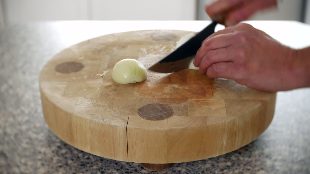 A chef is chopping onions in a kitchen on a chopping board with a knife