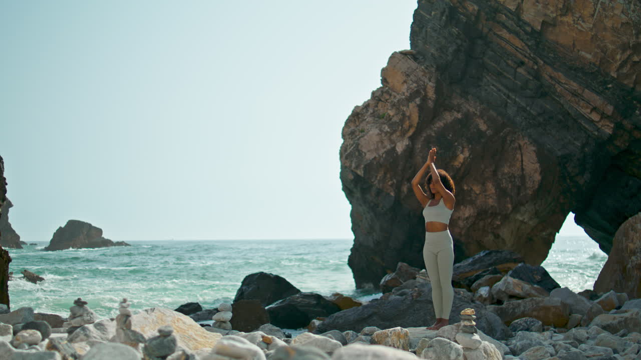 Ragazza che si allena con le mani alzate verso il cielo sulla riva del mare, in verticale. Donna in meditazione sulla spiaggia.