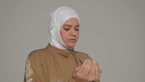 studio head and shoulders portrait of muslim woman wearing hijab praying