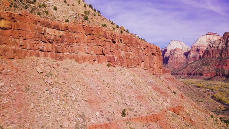 a drone flies past a rock wall to reveal a glorious valley and mountain range beyond