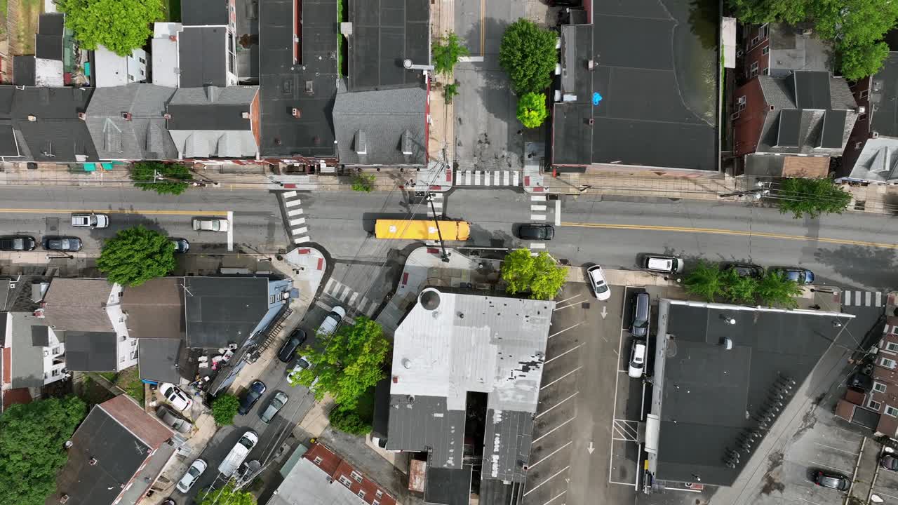 Yellow American school bus on road of town along townhouses and row homes. Sunny day in spring. Traffic scene in the morning. Lancaster, PA, United States. Aerial top down tracking.