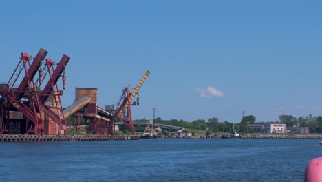 port cranes and harbor warehouses in sunny calm summer day at port of ventspils, venta river in front of frame, wide shot from a distance