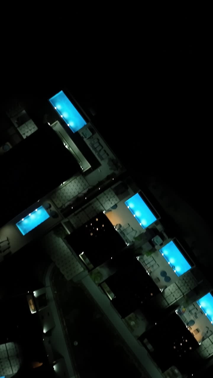 Vertical drone shot on top of illuminated pools and villas, night in Greece