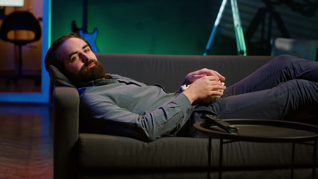 영화 를 보는 동안 소파 에 누워서 팝콘 을 먹는 미소 짓는 남자