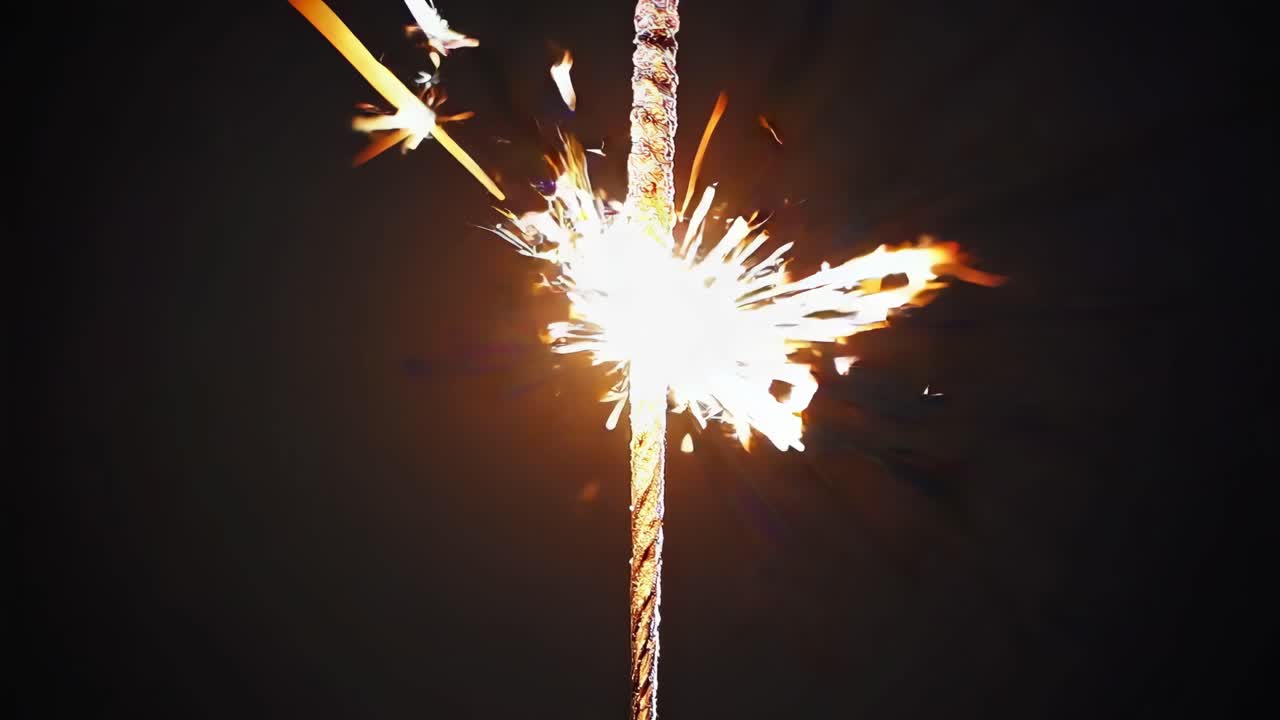 Close-up, eye-level shot of a sparkler emitting bright sparks against a dark background