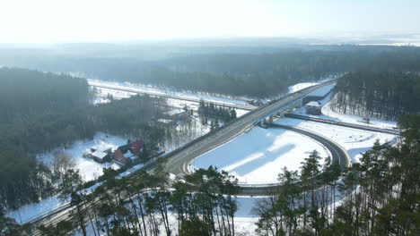 Toma-De-órbita-Aérea-De-La-Carretera-Nevada-Durante-El-Invierno-Y-El-Sol-Con-El-Tráfico-Cruzado-Y-La-Carretera-De-Salida