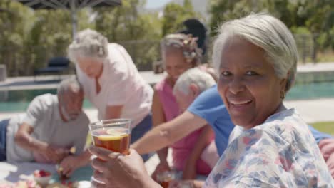 Smiling-diverse-senior-woman-and-friends-having-picnic-in-sunny-garden,-unaltered,-in-slow-motion