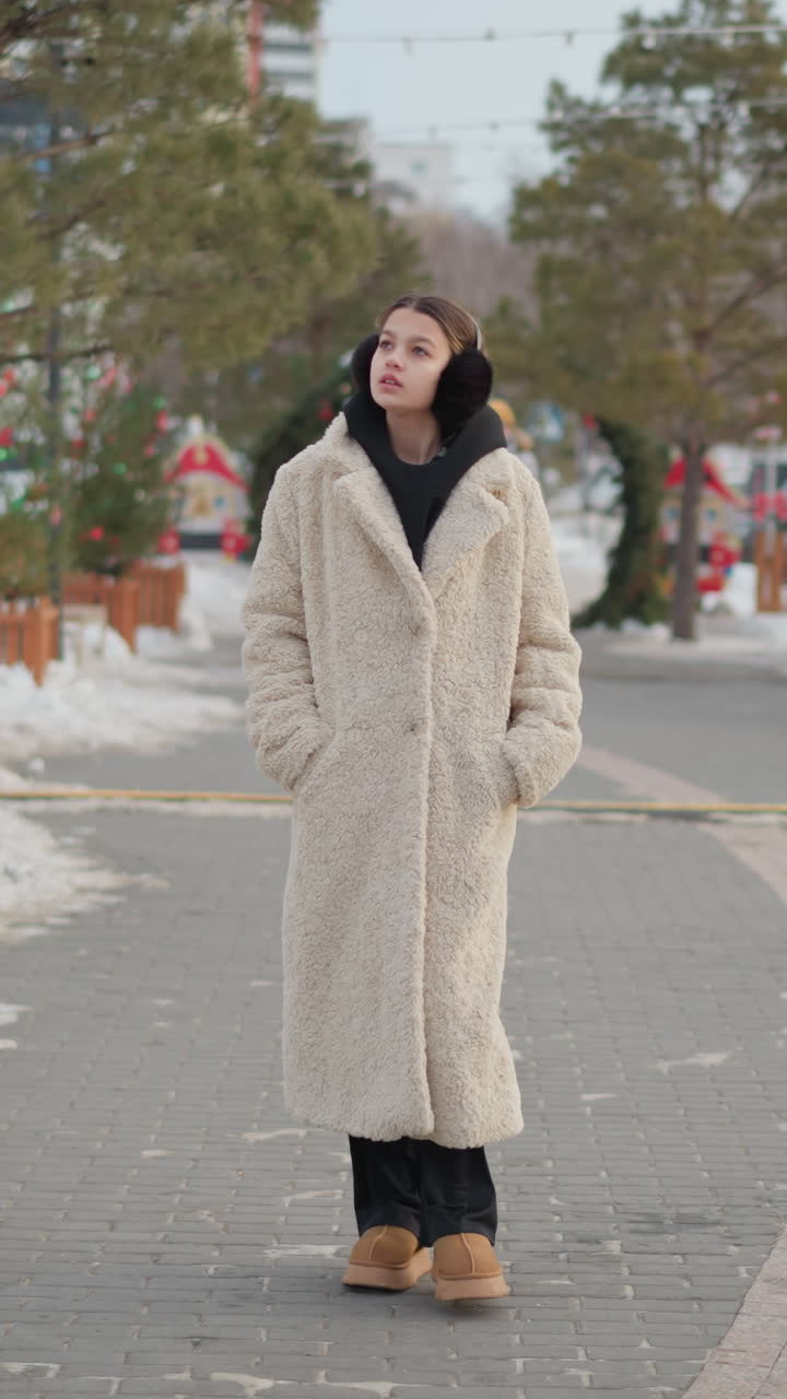 mujer joven y blanca paseando por un mercado de invierno, abrigo largo de borreguito, sudadera negra con capucha y orejeras, plaza cubierta de nieve con adornos festivos, ritmo lento y pausado, ambiente de retrato espontáneo, tonos neutros y con textura