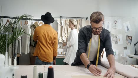 el joven diseñador toma medidas mientras un hombre y una mujer rubia eligen ropa en el fondo