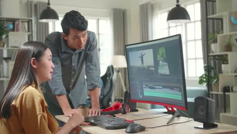 asian female video and sound editor works with her male colleague on a project on her personal computer. they work in a creative loft office