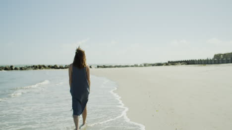 female fashion model walks along shore at the beach, sunny day, wide