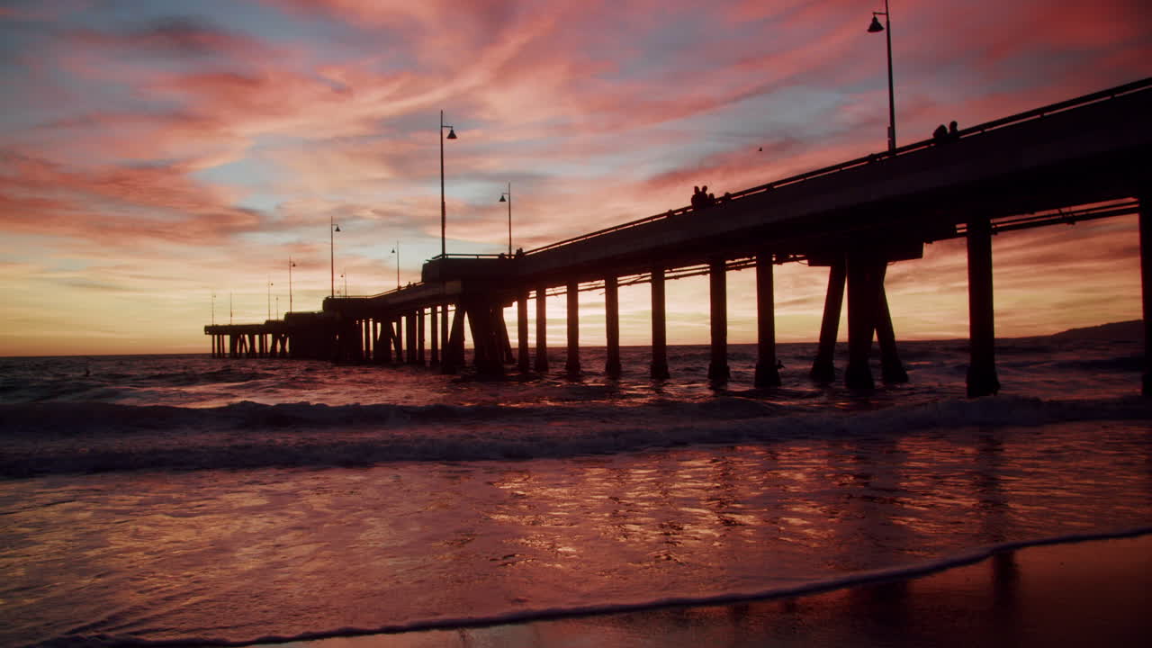 Vibrant Sunset over a Pier with Silhouetted Figures and Ocean Waves