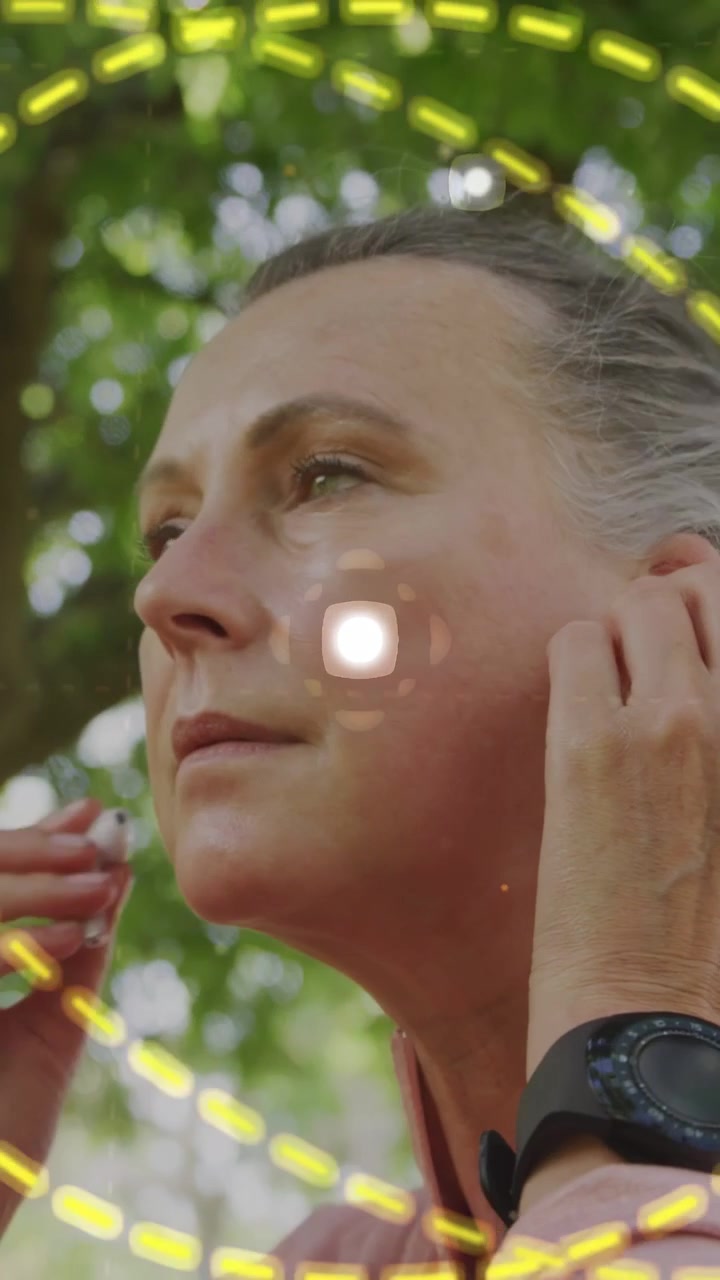 Video verticale: Donna che alza la mano inserendo gli auricolari e regolandoli in un parco, con anelli tecnologici che le circondano la testa.